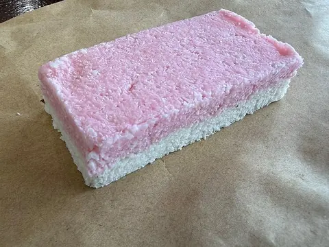 A pink and white layered coconut-ice bar on parchment paper