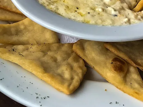 Golden triangular baked pita chips served with creamy artichoke dip